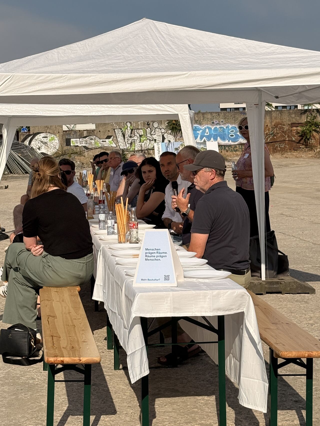 Invitados conversando en la Mesa Larga de la Baukultur bajo la carpa